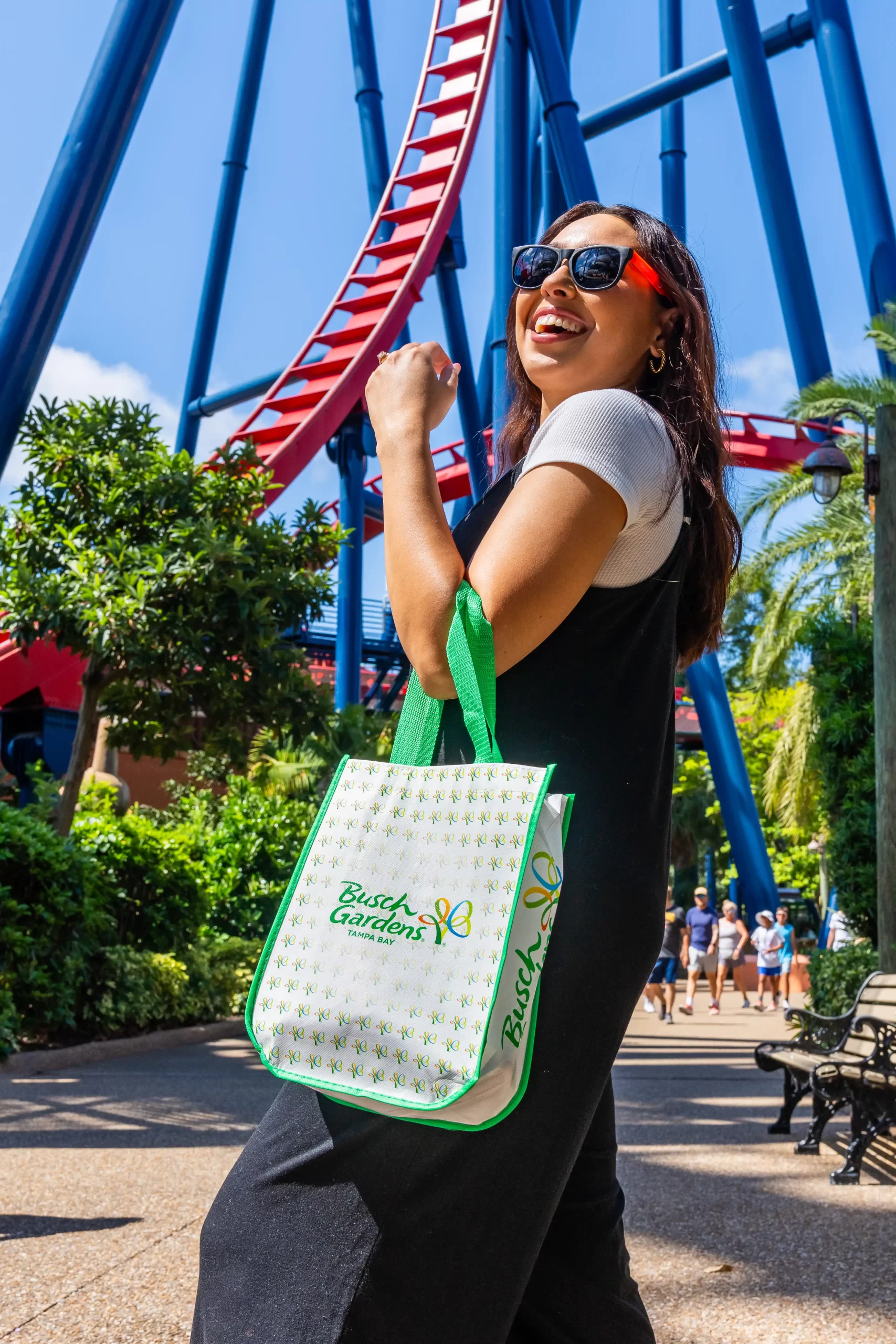 A guest carrying a white and green Busch Gardens tote bag past a roller coaster