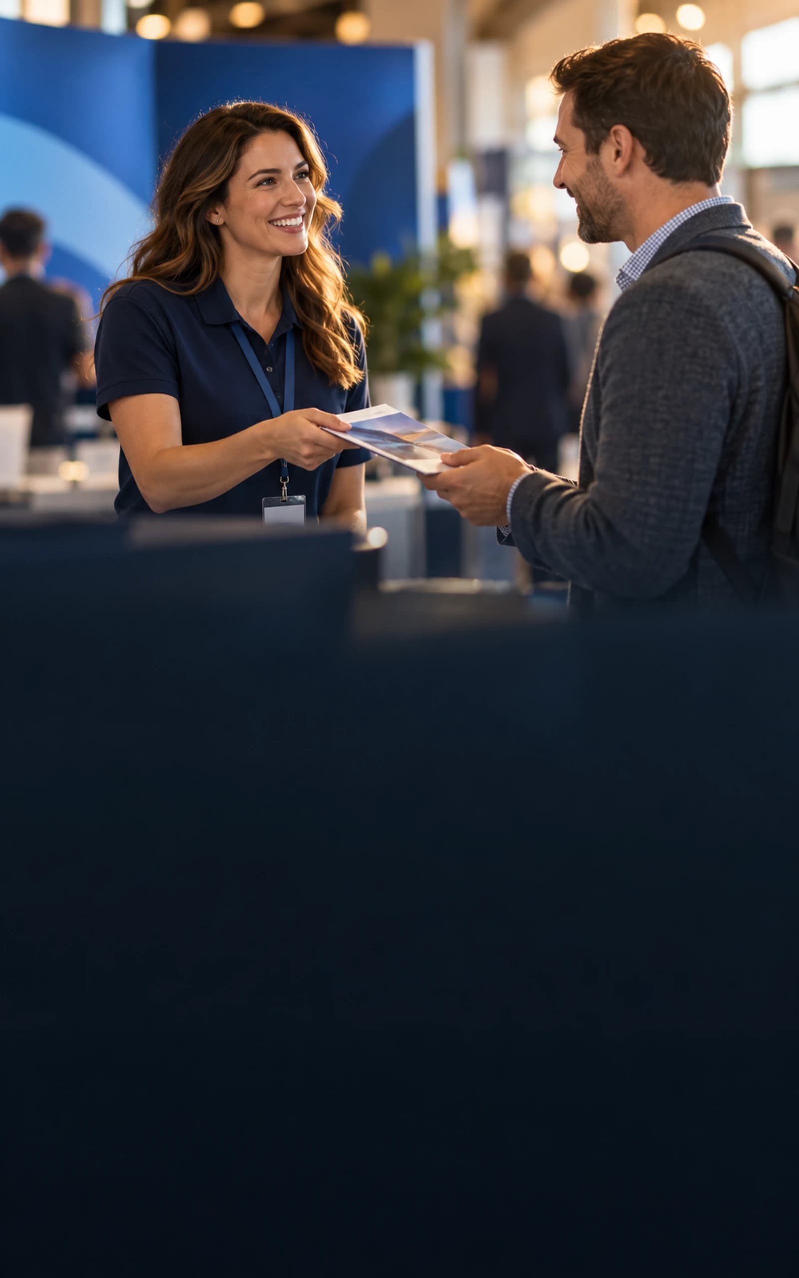 Cinematic lifestyle artwork of an exhibitor handing a printed brochure to a visitor at a coordinated trade-show booth