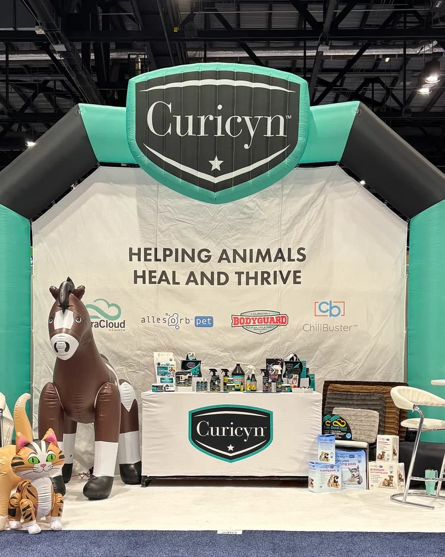 A trade show booth framed by a giant inflatable arch with the company's logo on top, and inflatable animals beside the table