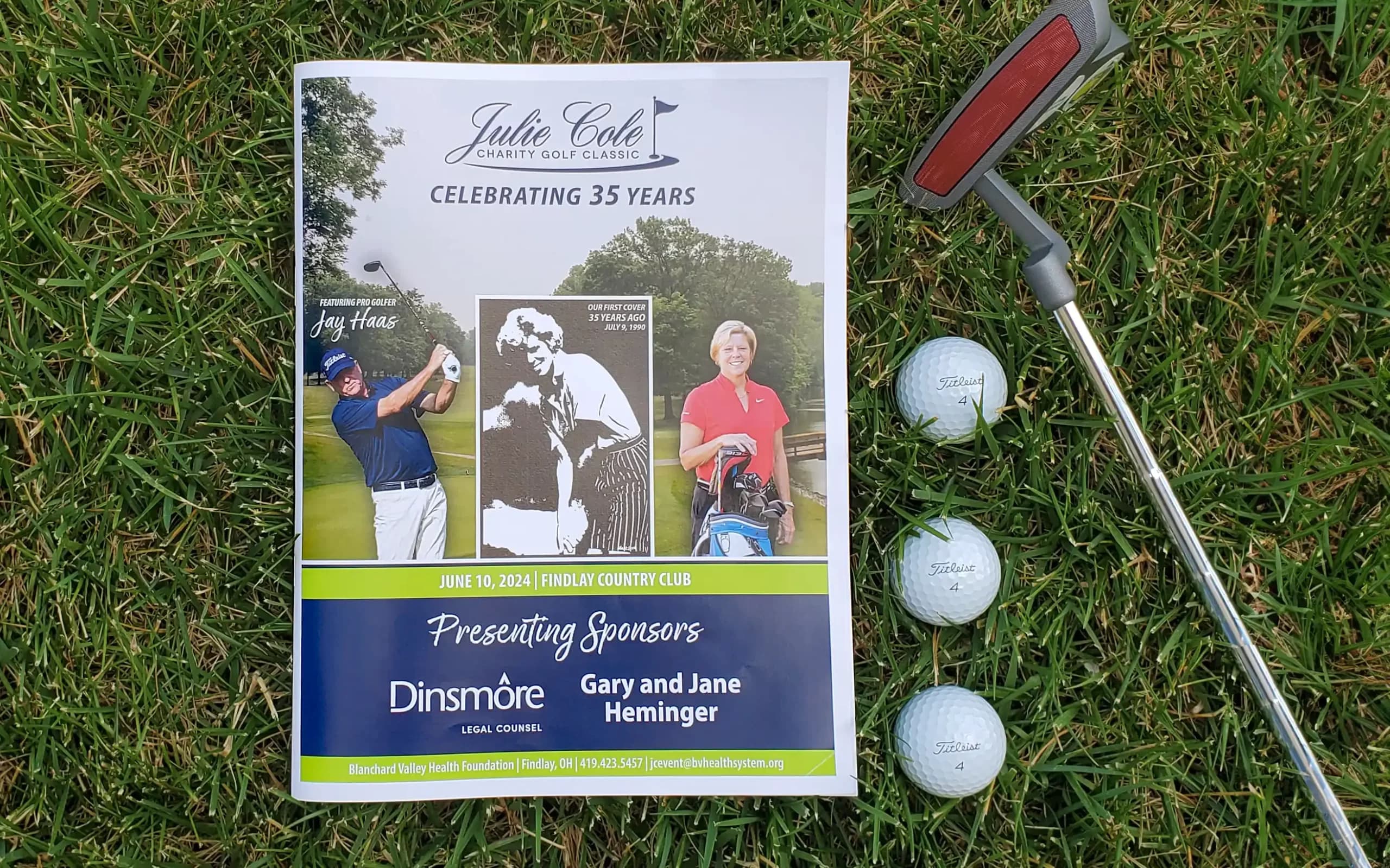 The printed program for the Julie Cole Charity Golf Classic on the grass beside a golf club and balls