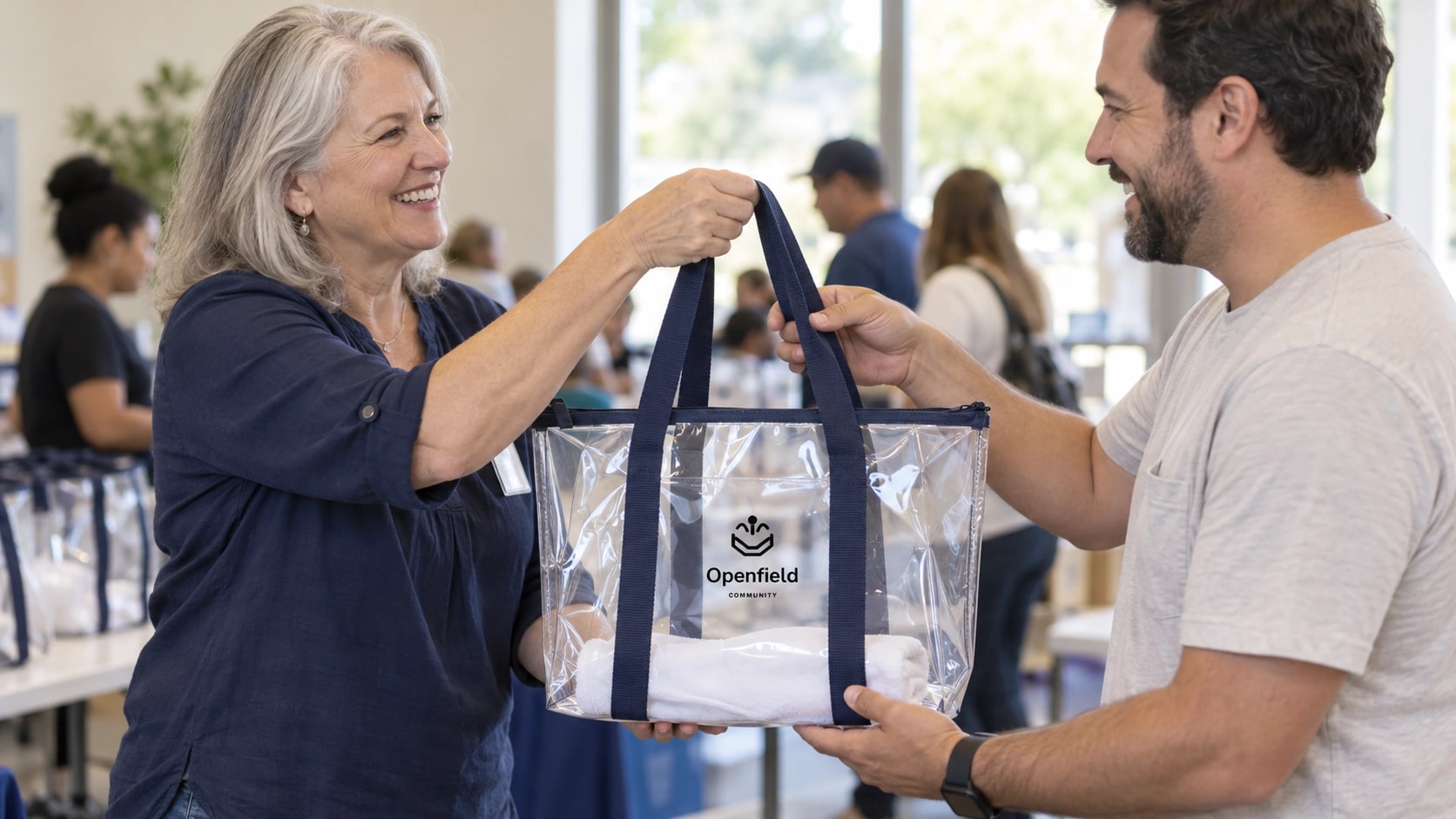 Illustrative scene of a volunteer handing a visitor a clear Laguna Beach tote with sample Openfield branding at a community event