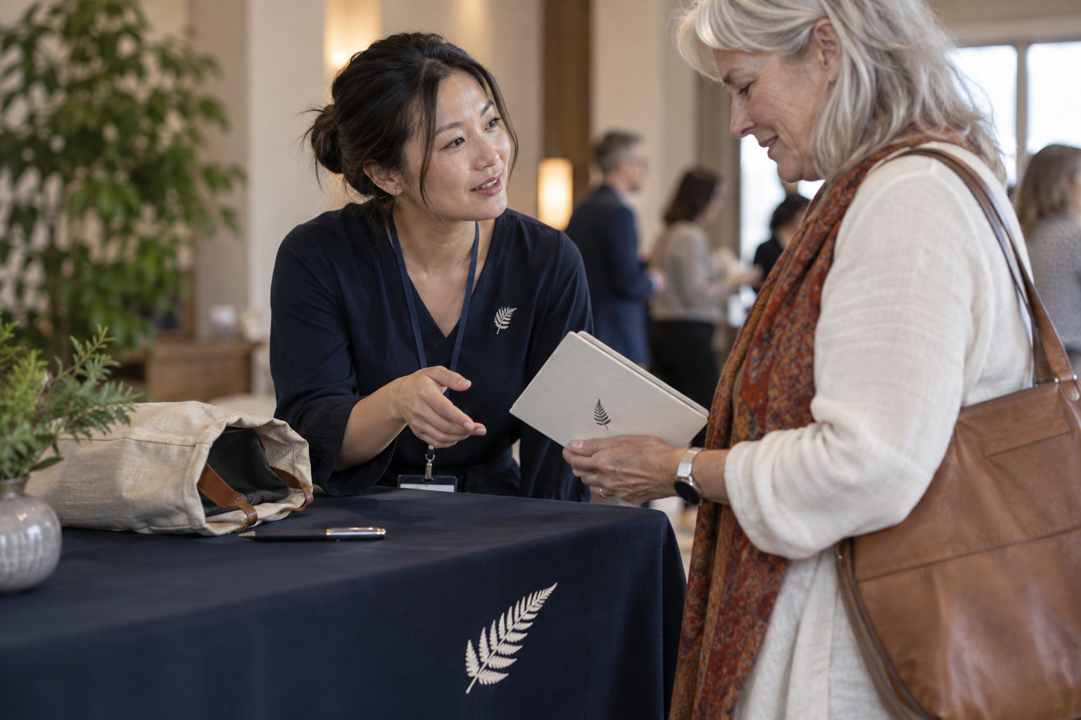 Cinematic artwork of a visitor holding a notebook while talking with an exhibitor across a table with a printed cover