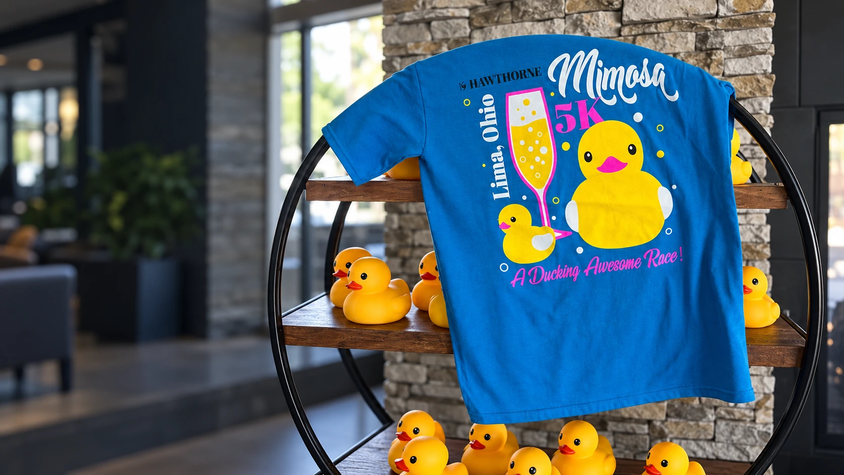 Cinematic artwork based on a customer photograph of a blue 19 Hawthorne Mimosa 5K shirt draped over a circular shelf with yellow rubber ducks