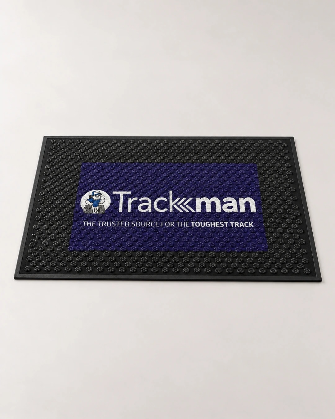 Cinematic artwork of a black Trackman rubber scraper mat with raised circular texture and a dark blue logo panel, based on the production proof
